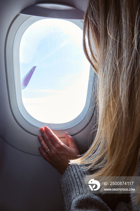 Woman looks out the window of an airplane. Hand near the porthole. Girl on the plane. Airplane wing, scenic view. Beautiful cloud, blue sky. Traveling by plane, adventure. Air transport. Aviation