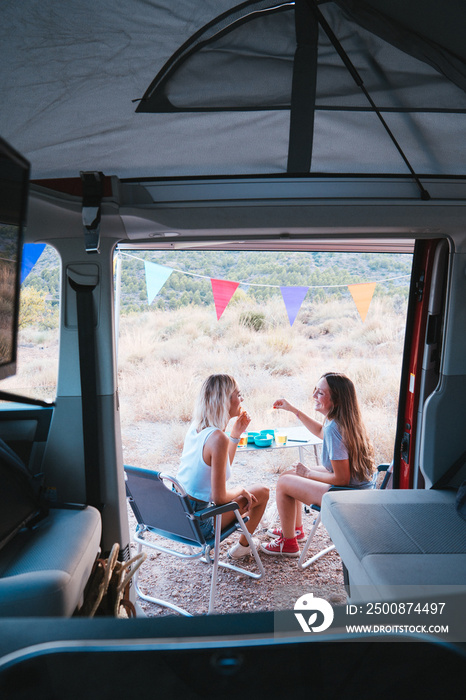 View from inside of camper van from a couple of women having a funny picnic in a mountain, during her road trip. Best friend.