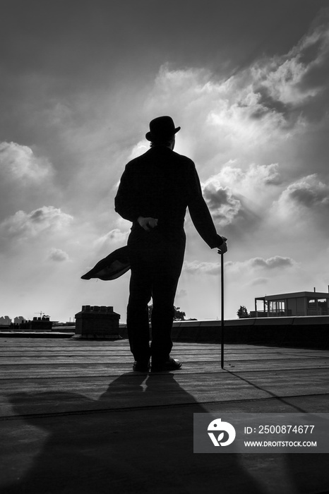 Black and white silhouette of a an elegant gentleman wearing a long a coattail with a cane and a  bowler hat