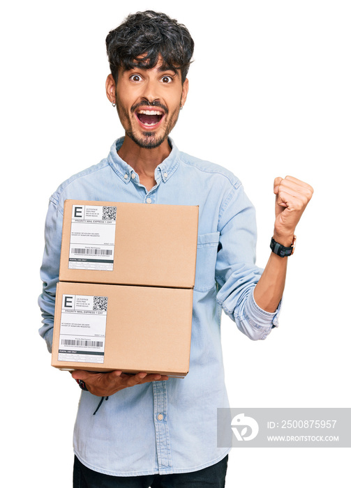 Young hispanic man holding delivery package screaming proud, celebrating victory and success very excited with raised arms