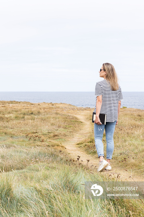 Woman walking along a path in front of the sea