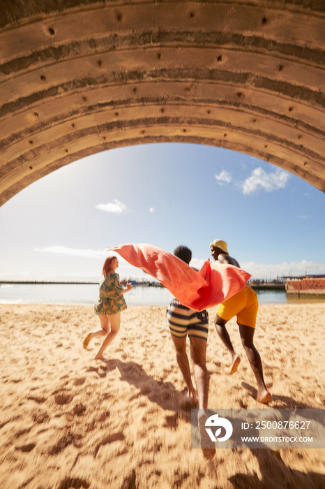 Young friends running through tunnel into water on harbor beach while on summer holiday