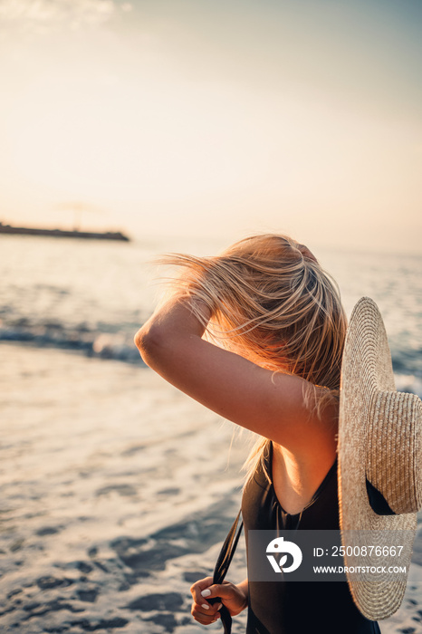 Young beautiful woman in a black swimsuit and hat with glasses walks along the beach in Turkey at sunset. The concept of sea recreation. Selective focus