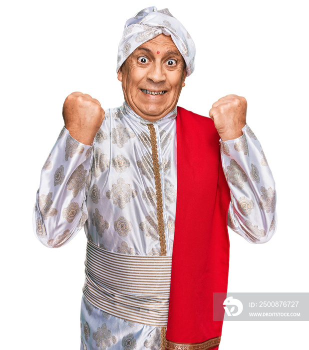 Senior hispanic man wearing tradition sherwani saree clothes celebrating surprised and amazed for success with arms raised and open eyes. winner concept.