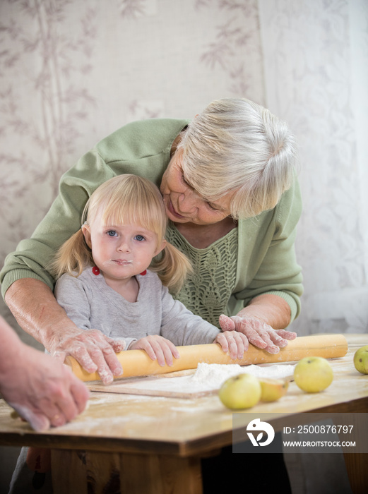 A grandmother making little pies with her granddaughter. Rolling the dough