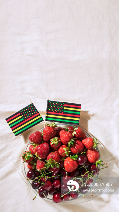 Juneteenth day picnic background with Black Liberation African American flags, sweet salad with cherries and strawberries, strawberry cheesecake