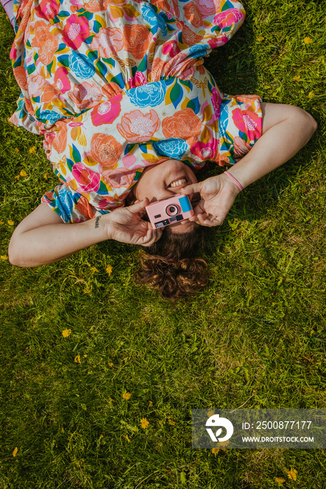 plus size woman lays on grass holding a pink camera