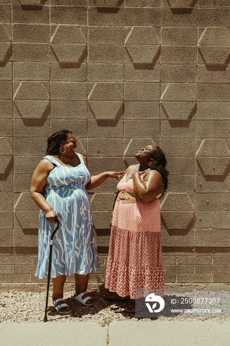 2 plus size African American women talk and laugh standing against a wall