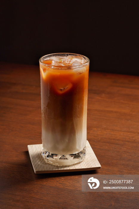 glass of iced coffee two layers fresh milk and espresso short on wooden table in dark background. Refreshing summer drink concept. (close up, selective focus)