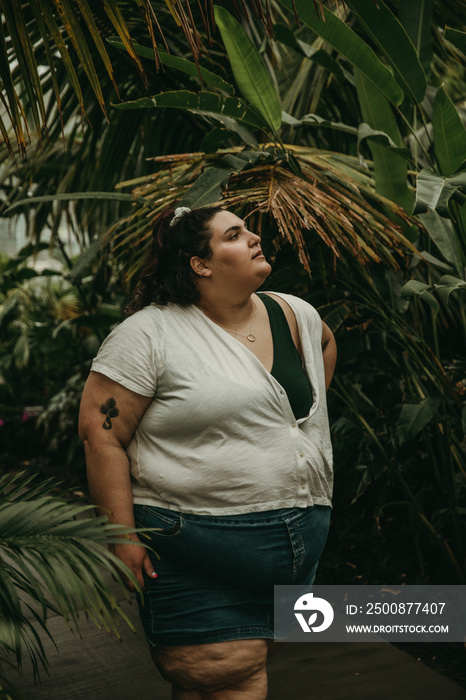 plus size woman walks in forest and looks up at plants