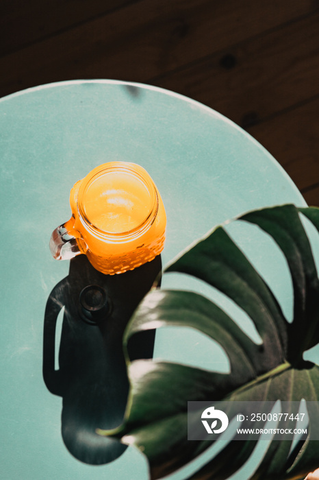 fresh orange juice in summer light and monstera or split-leaf philodendron leaves