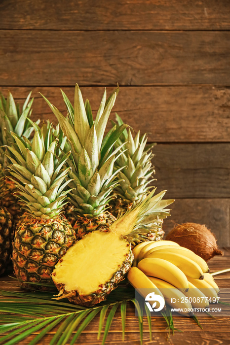 Ripe pineapples, bananas and coconut on wooden background