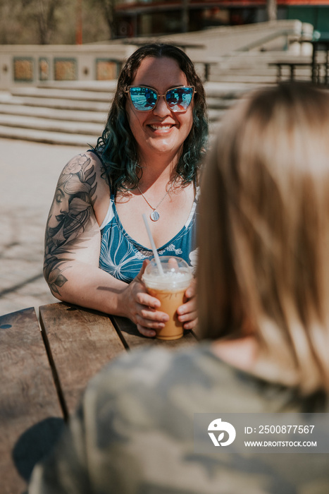 2 women talk and drink coffee outside