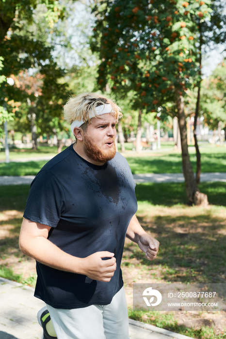 Young overweight man running outdoors in the park during his sport training