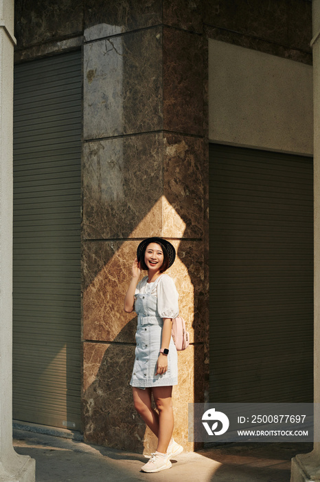 Full-length portrait of lovely Asian woman in summer hat posing in the street