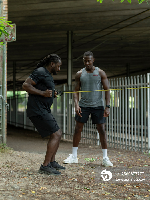 Two men doing strength training with resistance band outdoors