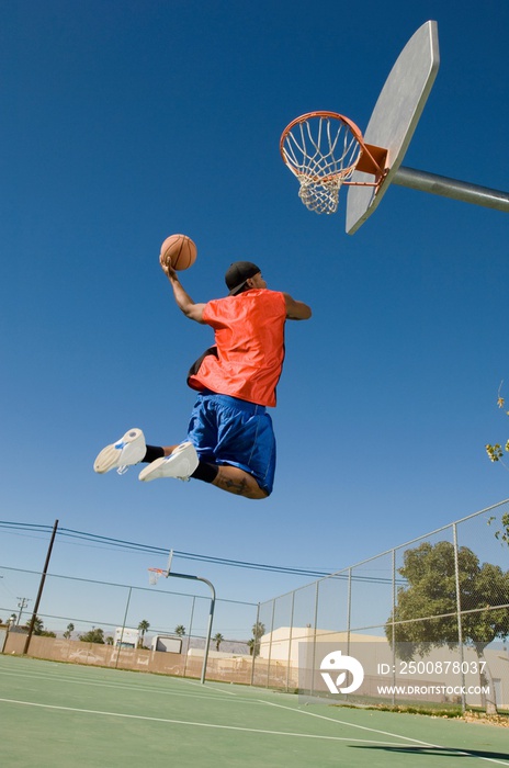 Man Dunking Basketball Into Hoop Against Blue Sky