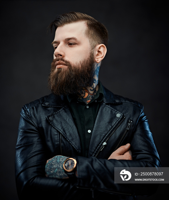 Portrait of a tattooed cool bearded man in a leather jacket with arms crossed