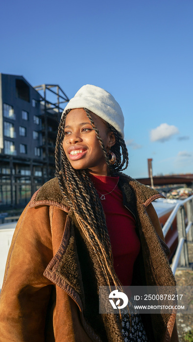 Portrait of smiling young woman with braided hair and cap outdoors