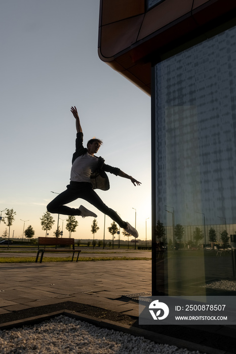 young attractive dancer in casual cloth doing ballet jump on the urban background. Contemporary dance, modern choreography.