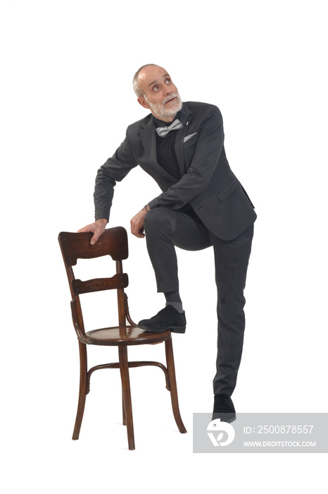 man in a bow tie and suit plays with a chair and looks up on white background