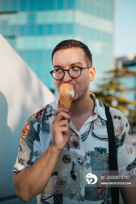 Young fashionable man eating ice cream in a cone in the city at sunset