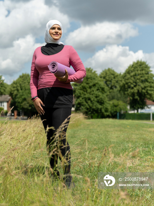 UK,Sutton,Portrait of woman in headscarf standing in meadow with yoga mat