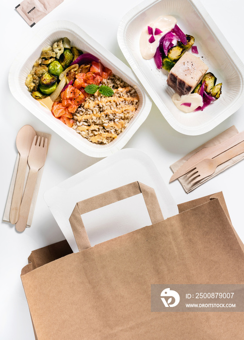 Collection of white plastic take away boxes with healthy food. Set of containers with everyday meals - meat, vegetables and law fat snacks on white background . wooden cutlery and a paper bag