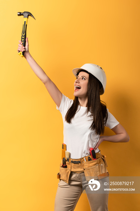 happy handywoman holding hammer and screaming on yellow background