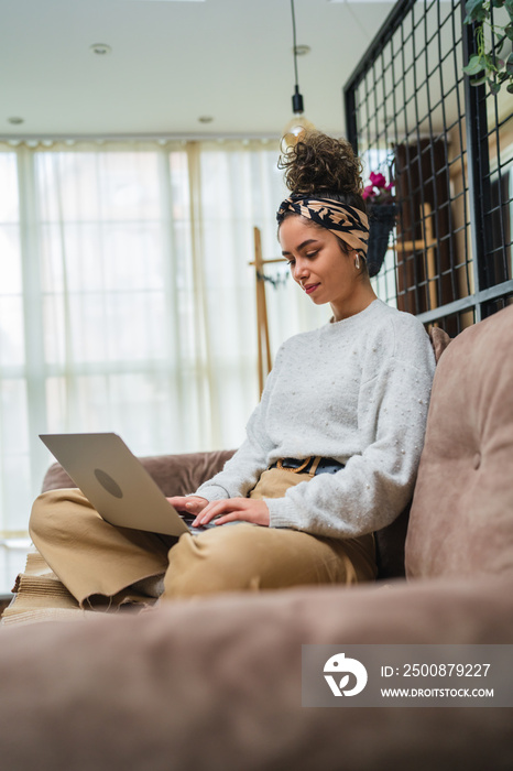 A young girl studying or doing business from her home while sitting on sofa and working on her laptop and drinking coffee during the day