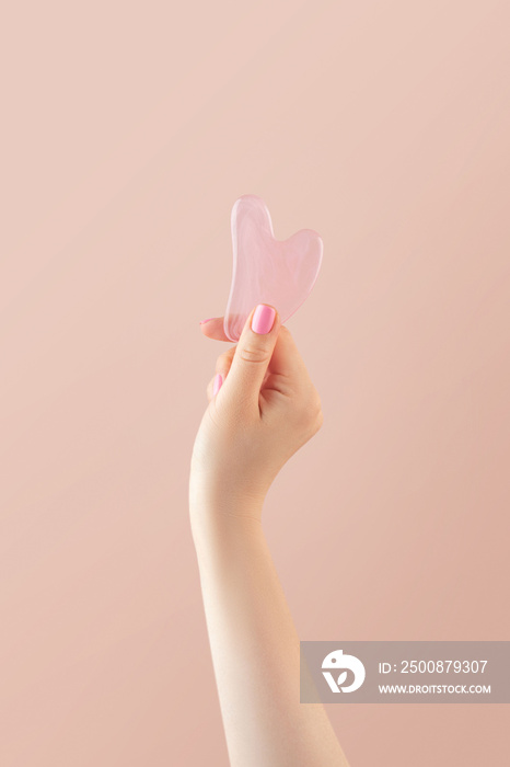 A woman holds a gouache jade massage scraper in her hand. Trendy beauty treatments. Copy space.