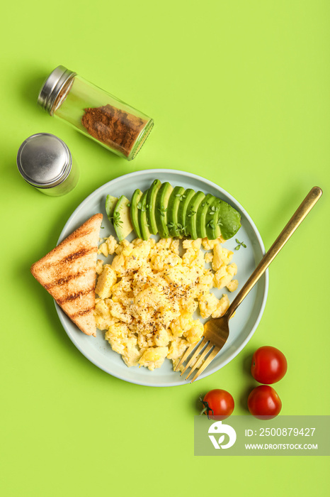 Plate with tasty scrambled eggs, avocado, toast, tomatoes and spices on green background