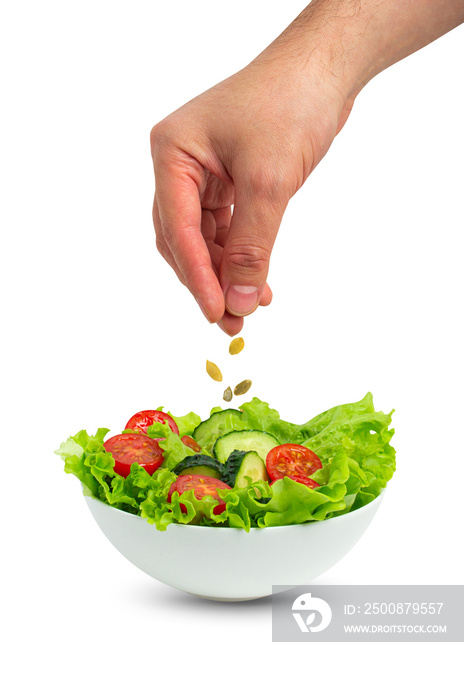 White bowl of salad with fresh cucumbers, tomatoes, iceberg salad leaves and male hand pouring oil with spoon over salad isolated on white background