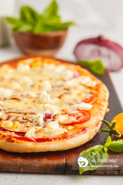 Oval homemade pizza with feta cheese, tomatoes and basil on a wooden board.