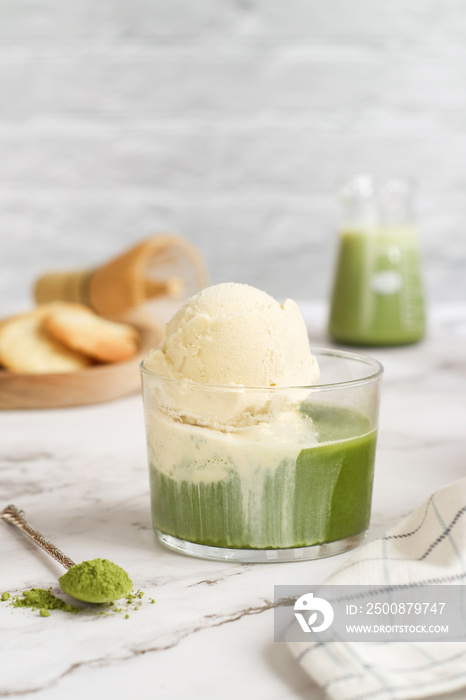 A glass of matcha affogato with vanilla ice-cream on the top of green tea with ice and its powder on spoon with cookie in bright background. A healthy antioxidant food and drink concept