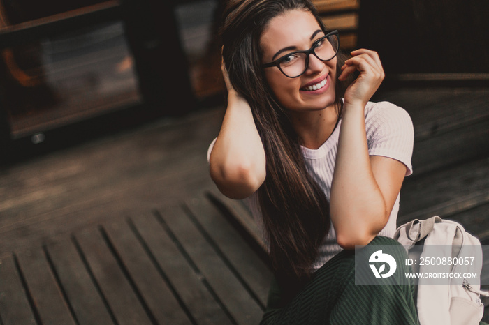 Happy smiling woman in glasses sitting on wooden steps in street.