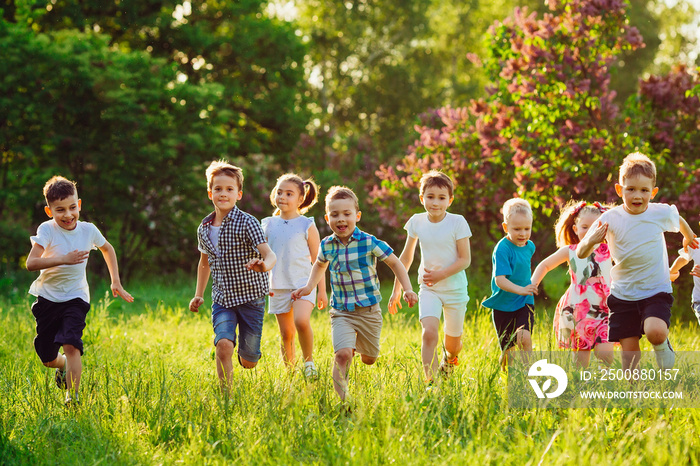 A group of happy children of boys and girls run in the Park on the grass on a Sunny summer day.