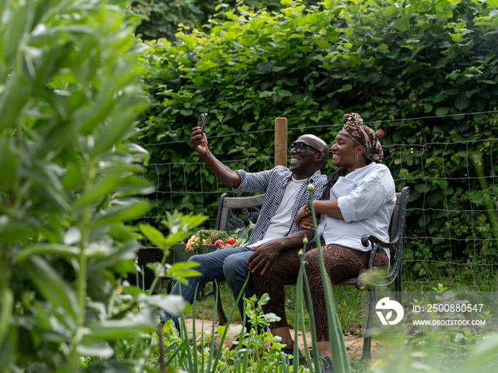 Smiling couple taking selfie on bench after working in garden