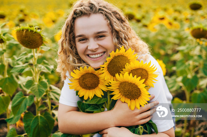 Happy farmer woman hugging some sunflower flowers, enjoying a rich harvest. Natural beauty. Summer nature. Smiling girl.