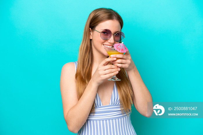 Young woman isolated on blue background in swimsuit and holding a cocktail