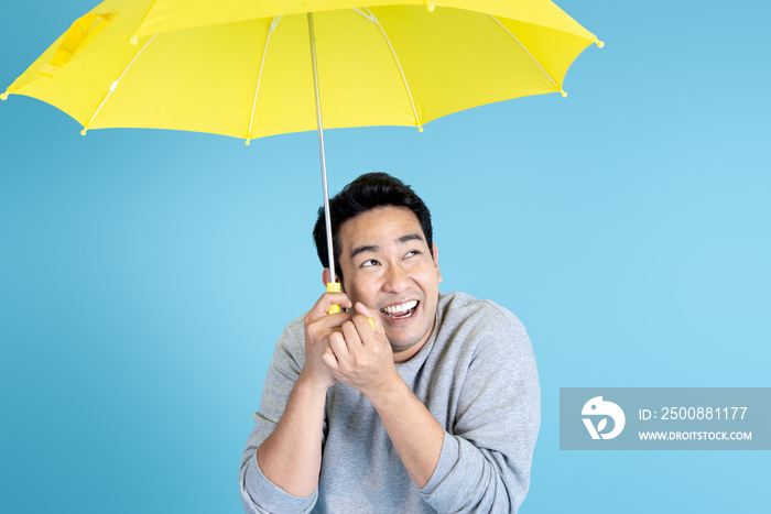 Happy Asian man holding yellow umbrella on blue background.