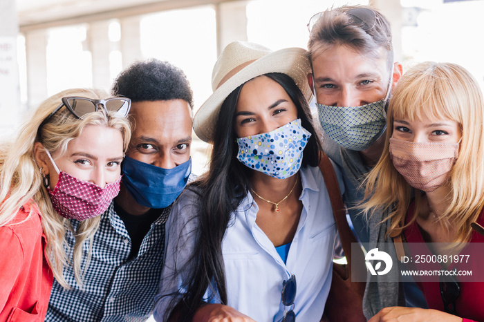 Portrait group of young happy friends wearing face mask during Covid pandemic smiling at the camera. Multiracial people taking a selfie outdoor having fun together. New normal lifestyle concept.