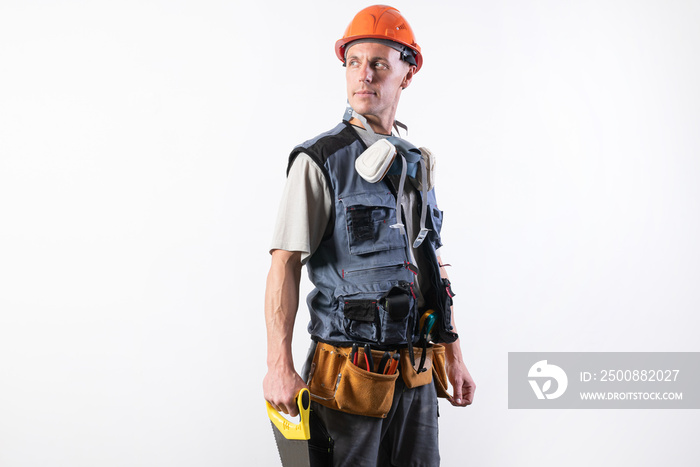 The builder in a helmet, and unloading, holds a hacksaw in his hands on a tree. On a light background.