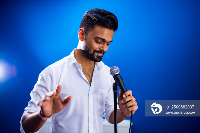 indian man in white shirt with beard singing in recording studio on blue background