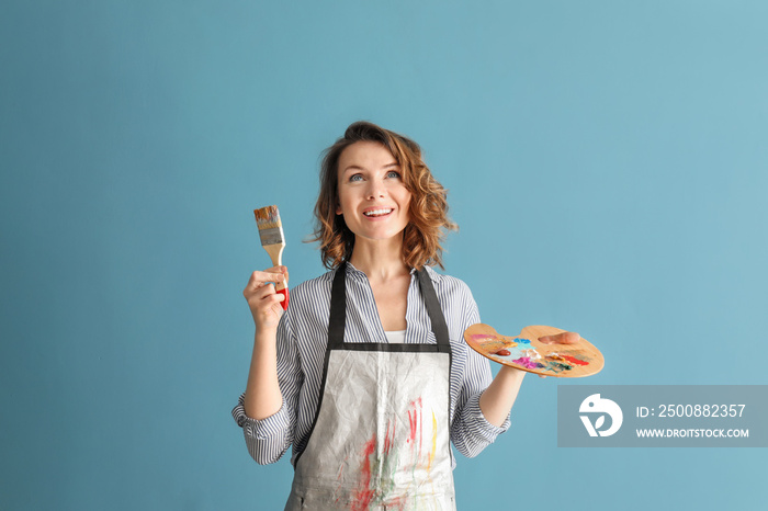 Female artist with brush and paint palette on color background