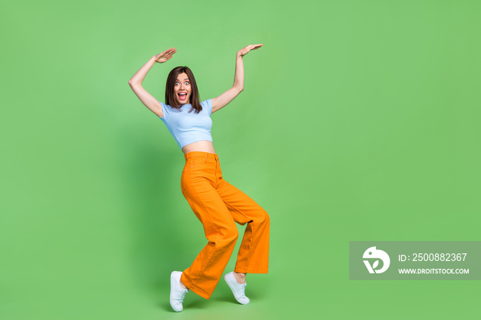 Full body portrait of overjoyed cheerful lady stand tip toe hands make moves dance isolated on green color background