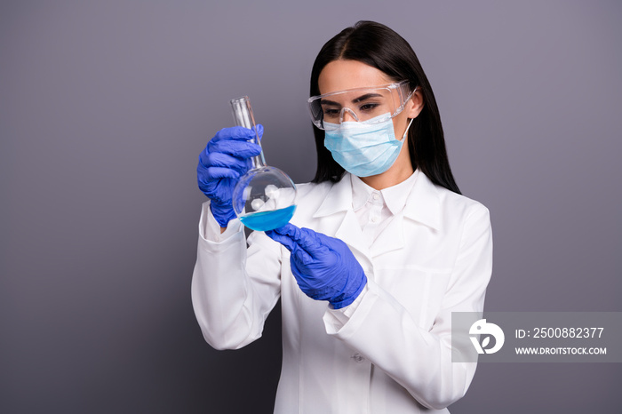 Portrait of concentrated scientist woman work in lab make new vaccine analyze chemical blue liquid hold flask wear white coat mask gloves goggles isolated over grey color background