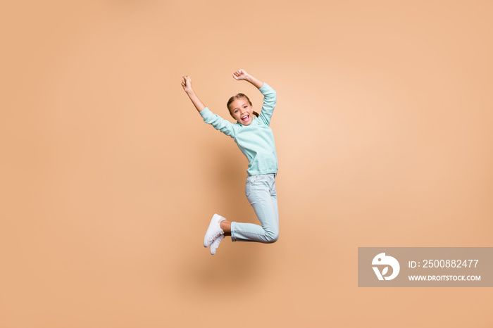 Full body profile photo of beautiful funny little lady jumping high up cheerleader celebrating winning raise fists wear blue sweater jeans footwear isolated beige color background