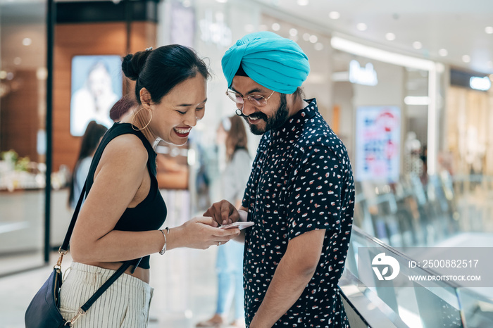 Happy Couple Using Mobile Phone Together At The Shopping Mall