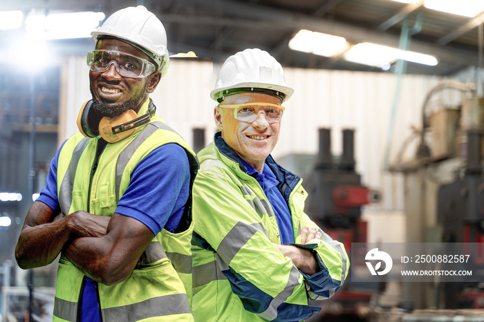 African man and senior man workers engineering standing with confident with blue working suite dress and safety helmet in front of indoor factory. Concept of smart industry worker operating.